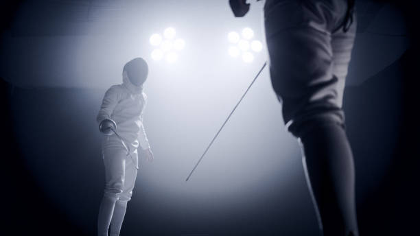 istock Two professional fencers foil swords facing each other in combat with epic blue stage lighting and smoke effects. Low angle view 1542473326
