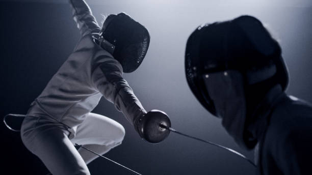 istock Two professional fencers foil swords facing each other in combat with epic blue stage lighting and smoke effects. Low angle view lunge 1542473337