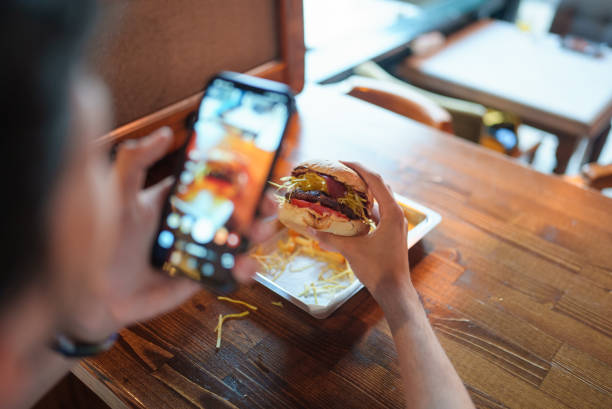 un jeune homme prend une photo de son hamburger avec son téléphone - photographing smart phone friendship photo messaging photos et images de collection