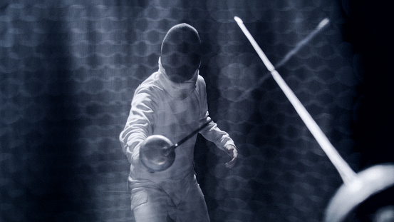 FPV two fencers dueling in a fencing sports match on lit-up stage. Foil swords clashing to determine the match winner