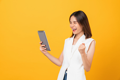 Studio shot of Beautiful Asian businesswoman holding digital tablet and smiling on yellow background.