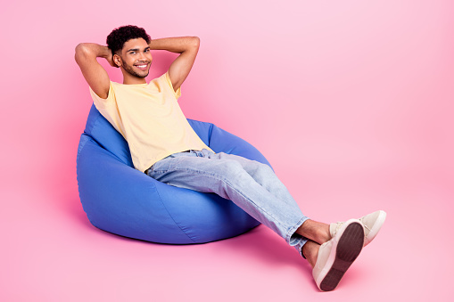 Full length body photo of young handsome guy sitting pouf hands head take nap pause relaxation rest isolated on pink color background.