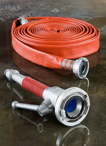 A rolled up firehose and a nozzle on the wet floor in a firestation used by firefighters