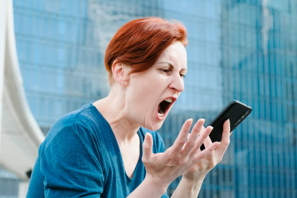 une femme aux cheveux courts tient un smartphone près de sa bouche et crie furieusement dans le micro - furiously photos et images de collection