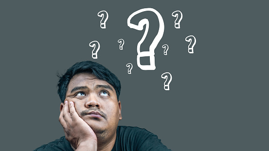 Asian young man sitting and wondering There is a question mark symbol on a gray background.