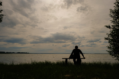 Black silhouette of a man with a backpack on the lake background.