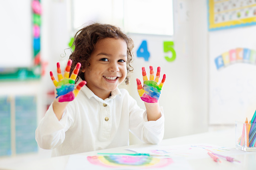 Child drawing rainbow. Paint on hands. Remote learning and online school art homework from home. Arts and crafts for kids. Little boy drawing bright picture. Creative kid playing and studying.