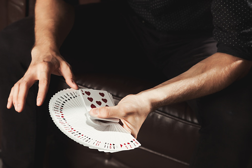 Close-up clever male hands of magician with gambling cards. Gambler man showing performing fan of cards. Concept of magic, performance, circus, gambling, casino, poker game, show. Copy ad text space