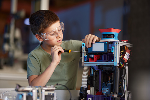 Small scientist repairing robotics part during his science project in laboratory.