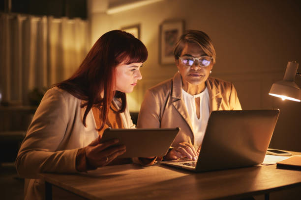 istock Remote work, night and teamwork by women working together in a partnership planning on a laptop for project. Tablet, internet and employees in collaboration working on a company strategy or proposal 1542573421