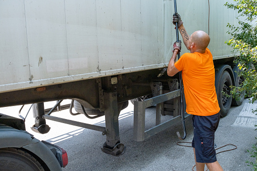 A large truck driver secures the trailer. He is wearing an orange T-shirt to be seen from a distance for security reasons.