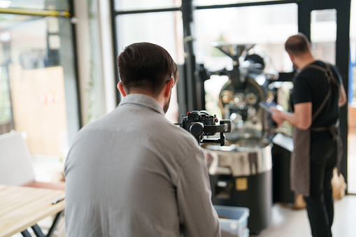 Man using camera and gimbal in coffee shop for social media, backstage