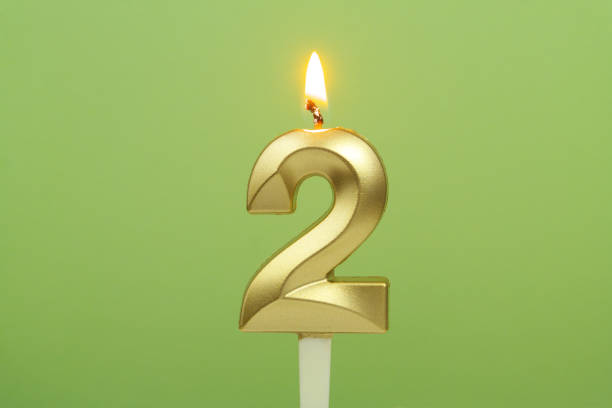 istock Gold birthday candle burning on green background. Number 2. 1542622812