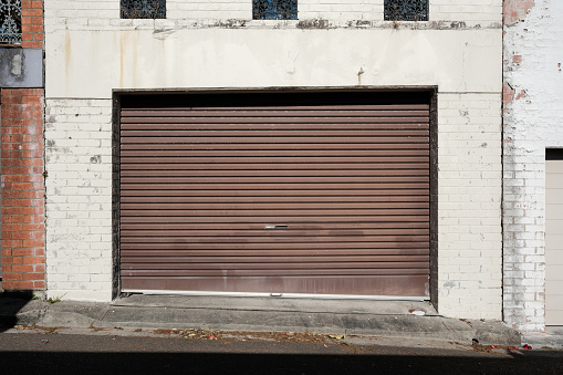 Old brown metal garage door with surrounding brick wall.