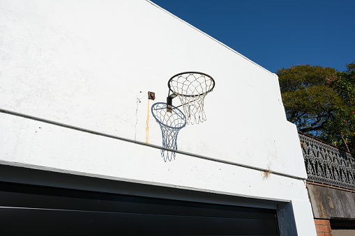 Old basketball hoop with net attached to a wall above a garage door.
