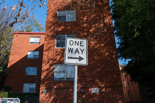 One way street sign on a metal pole with an apartment building behind.