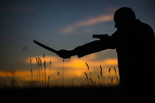 istock Silhouette of a demon and vampire hunter with a dramatic sky in the background. A man with a katana and a revolver. Fantasy and halloween concept 1542635111