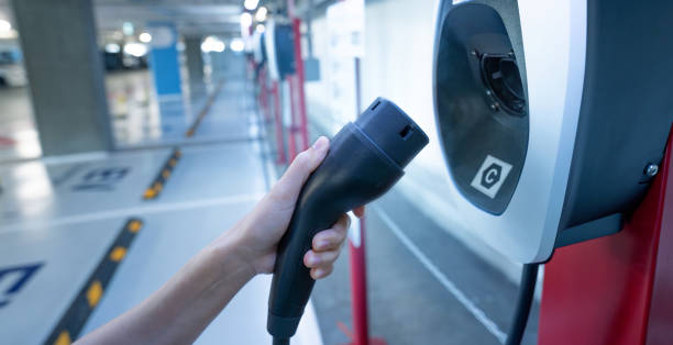 Hand holding electric charger at an electric vehicle charging station. Commercial EV car charging point for charge EV battery. Electric vehicle charging station at basement car parking lot of the mall sosteniendo el cargador eléctrico en una estación de carga de vehículos eléctricos. punto de carga comercial para coche ev para cargar la batería ev. estación de carga de vehículos eléctricos en el estacionamiento del sótano del centro comercial