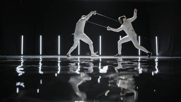 istock Two professional fencers foil swords dueling each other in combat with epic stage lighting. Dodging 1542655843