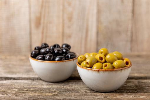 Green and black olives with leaves in bowls on a textured old wood background. Delicious and healthy food. Delicacy.Mediterranean Kitchen. Place for text. copyspace.