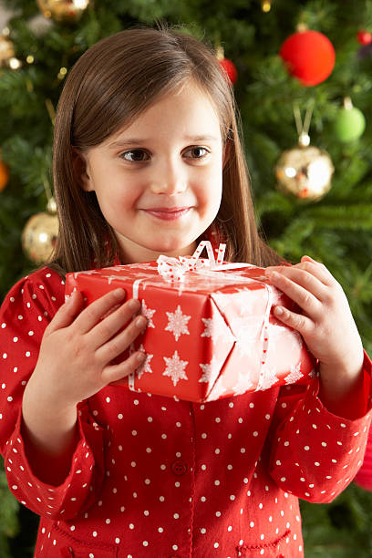 istock Young Girl Holding Gift In Front Of Christmas Tree 154265965