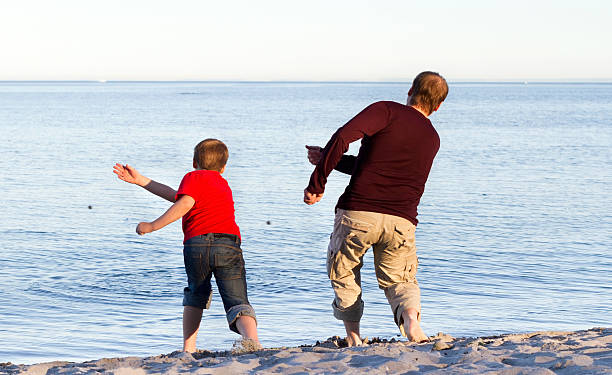 Father and son throwing pebbles into the sea stock photo