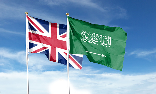 Union Jack and Saudi Arabia flag on cloudy sky. fluttering in the sky