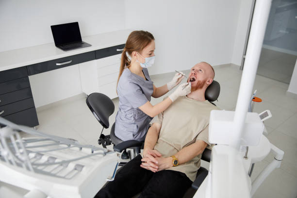 portrait of young female dentist standing by mid adult man in clinic. female dentist repairing patient tooth in dental ambulant - ambulant patient imagens e fotografias de stock