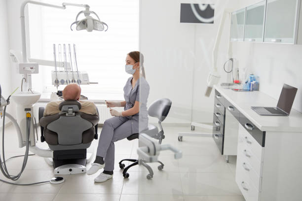 portrait of young female dentist standing by mid adult man in clinic. female dentist repairing patient tooth in dental ambulant - ambulant patient imagens e fotografias de stock