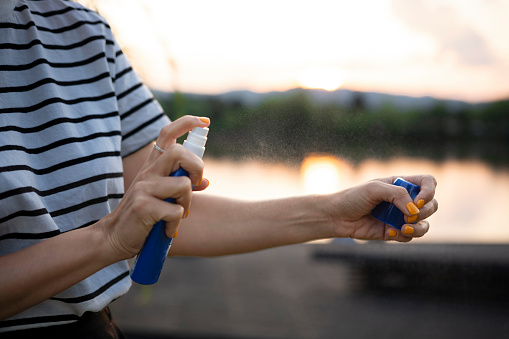 A woman sprays herself with mosquito repellent.