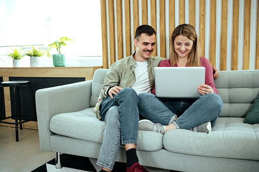 Couple using laptop together on sofa to shop online at home
