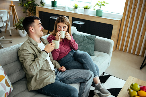 Couple is sitting on a sofa, talking and drinking coffee