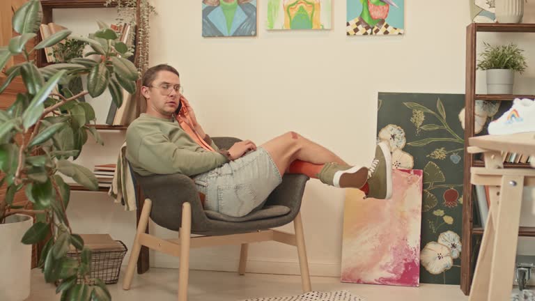 Male Designer Sitting in Armchair Talking on Smartphone in Loft Studio