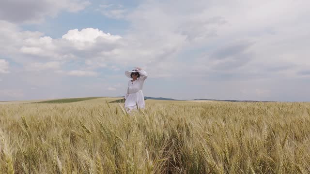 Happy woman in white dress and hat running on wheat agriculture harvest field, slow motion