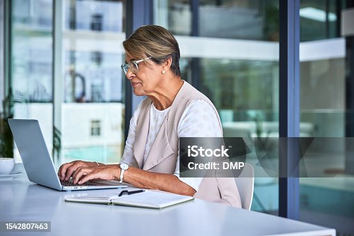 istock Laptop, typing and senior woman at desk, secretary doing research for office management and online schedule. Internet, computer and elderly receptionist working on report for administration business. 1542807463