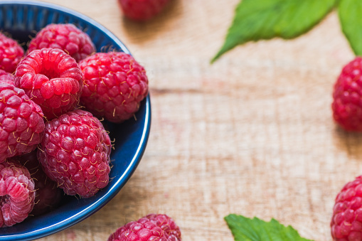 Fresh raspberries in a small blue bowl on a chopping board, copy space. Fruits on a wooden surface.