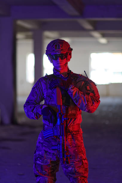 un soldado profesional emprende una peligrosa misión en un edificio abandonado iluminado por luces azul neón y púrpura - airsoft fotografías e imágenes de stock