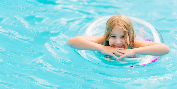 Cute and funny blonde teenage girl in a swimsuit with an inflatable lifebuoy swims in the pool. Safe rest with children by the water. travel and tourism.