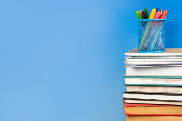 istock Composition with vintage old hardback books, diary and open book whith cup for pens and pencils on wooden table and blue background. Books stacking. Back to school. Copy Space. Education background. 1542876420