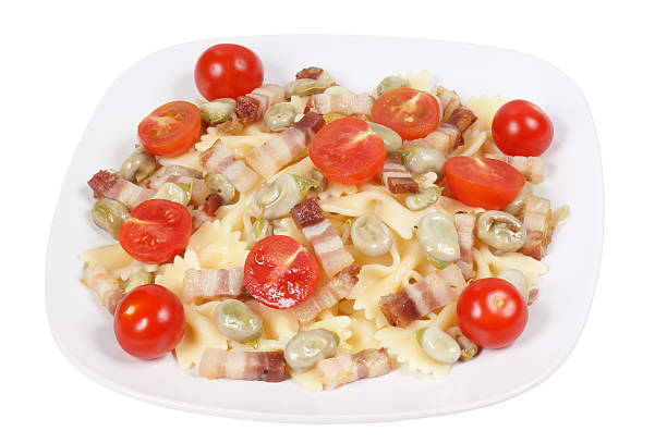Italian pasta: farfalle with broad beans, smoked bacon and cherry tomatoes. Studio shot. Isolated on white with clipping path.