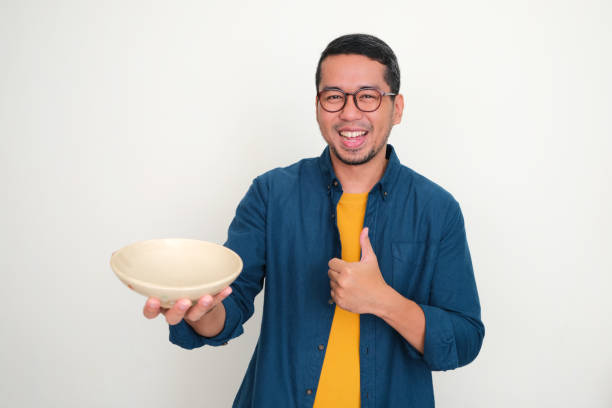 istock Adult Asian man smiling and give thumb up while showing empty dinner bowl 1542912591