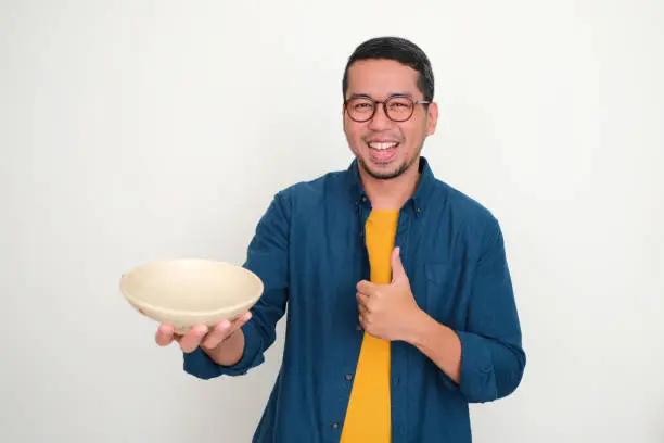 Adult Asian man smiling and give thumb up while showing empty dinner bowl