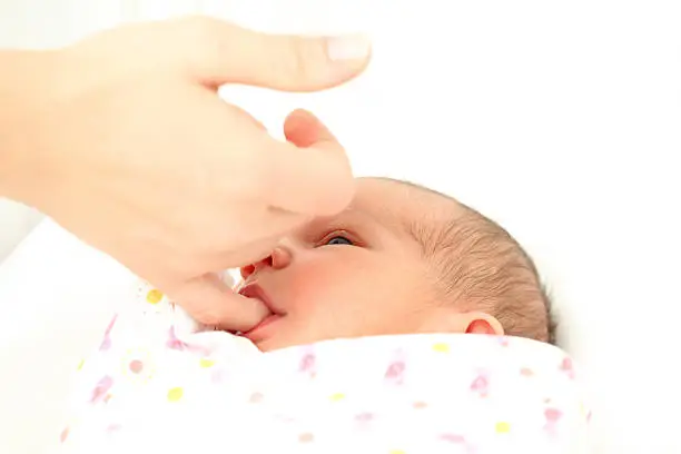 Newborn baby sucking on mothers finger