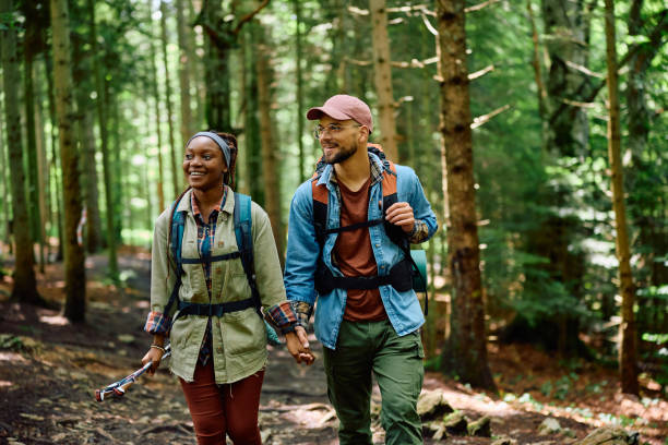 feliz pareja de excursionistas tomados de la mano mientras caminaban por el bosque. - mochilero fotografías e imágenes de stock