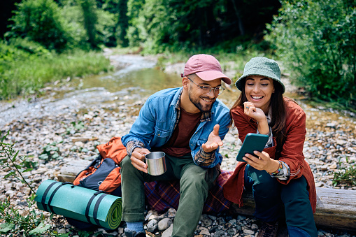 Happy couple of hikers using cell phone while relaxing in the forest.