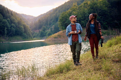 Happy man and his African American girlfriend walking by the lake in nature. Copy space.