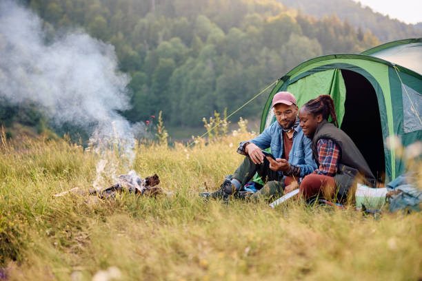 istock Happy couple using mobile phone while camping in nature. 1542962277