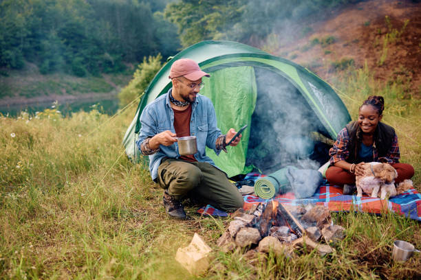 istock Happy man using cell phone while camping with his girlfriend and dog in nature. 1542964185