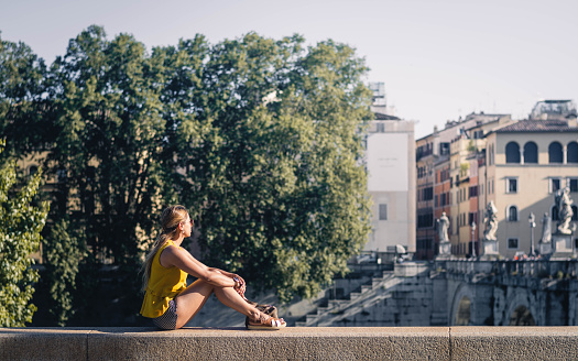 young woman sitting on the edge of a concrete railing looking at the landscape and architecture of a European city.