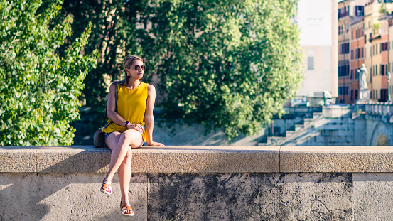 young woman sitting on a bridge in rome, waiting quietly for her romantic date.
